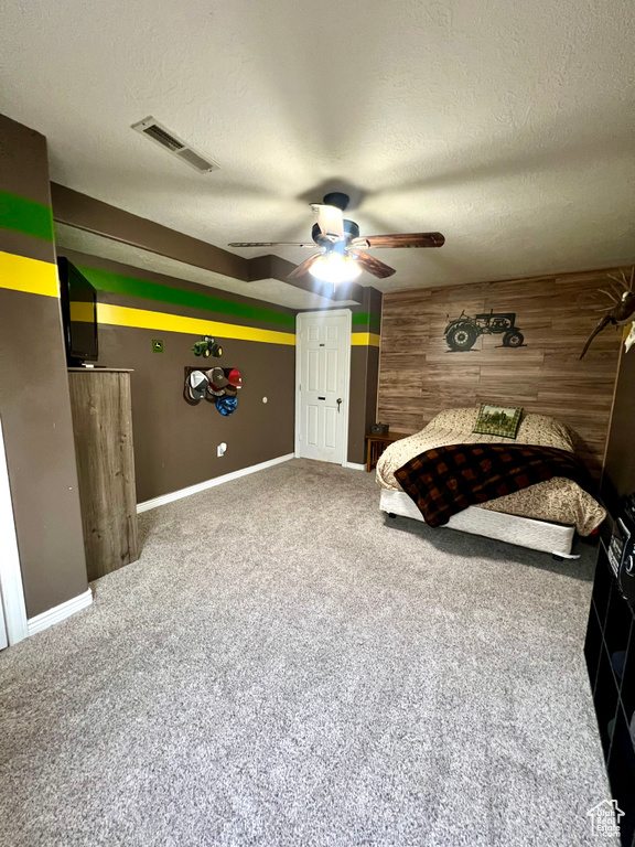 Bedroom featuring a textured ceiling, carpet flooring, wood walls, and a ceiling fan