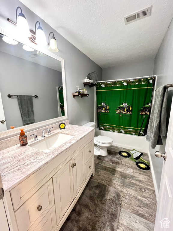 Full bath with shower / bath combination with curtain, vanity, a textured ceiling, and wood finished floors