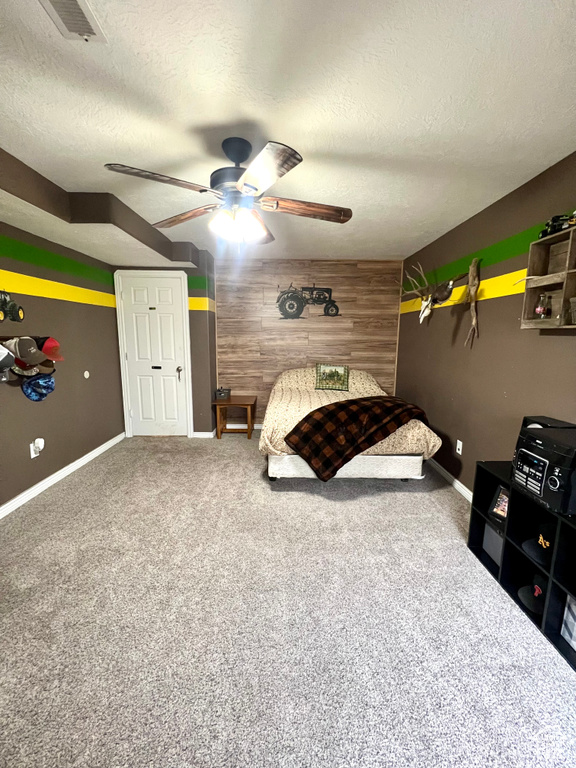 Bedroom featuring a textured ceiling, wooden walls, carpet flooring, and a ceiling fan