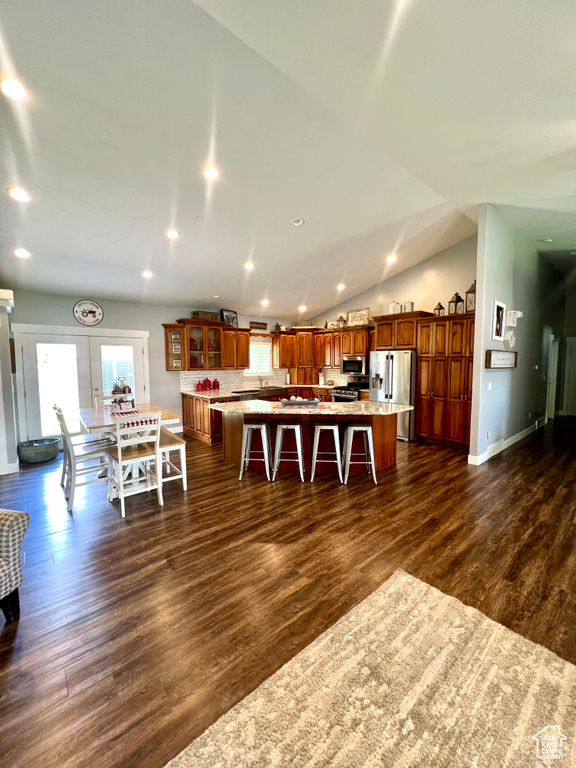 Kitchen featuring appliances with stainless steel finishes, a kitchen bar, brown cabinetry, dark wood finished floors, and recessed lighting