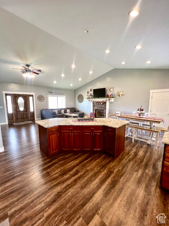 Kitchen with open floor plan, reddish brown cabinets, dark wood-style flooring, a fireplace, and lofted ceiling