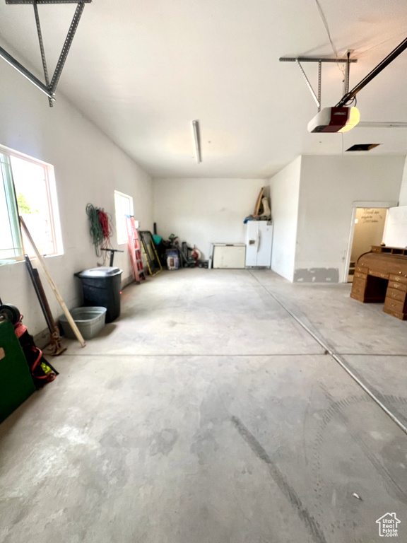 Garage with a garage door opener and white refrigerator with ice dispenser