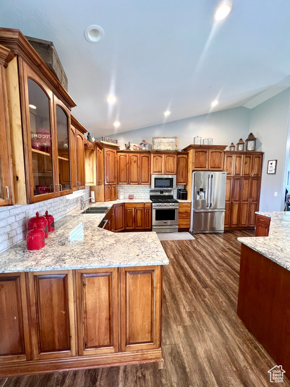 Kitchen featuring stainless steel appliances, vaulted ceiling, decorative backsplash, dark wood finished floors, and glass insert cabinets