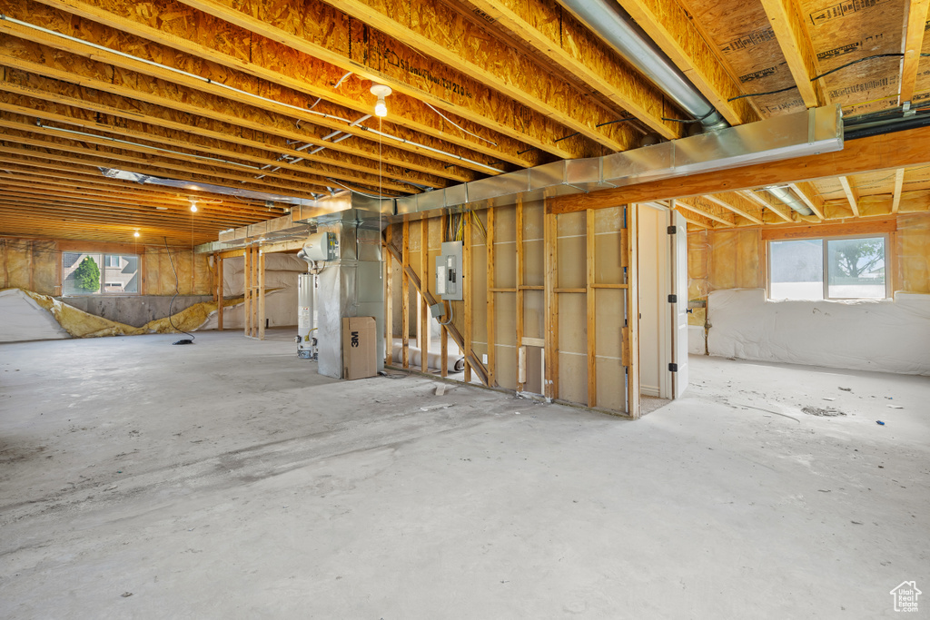Below grade area with electric panel, plenty of natural light, heating unit, and gas water heater