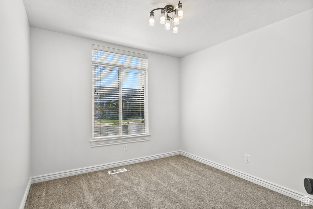 Carpeted spare room with baseboards and a chandelier