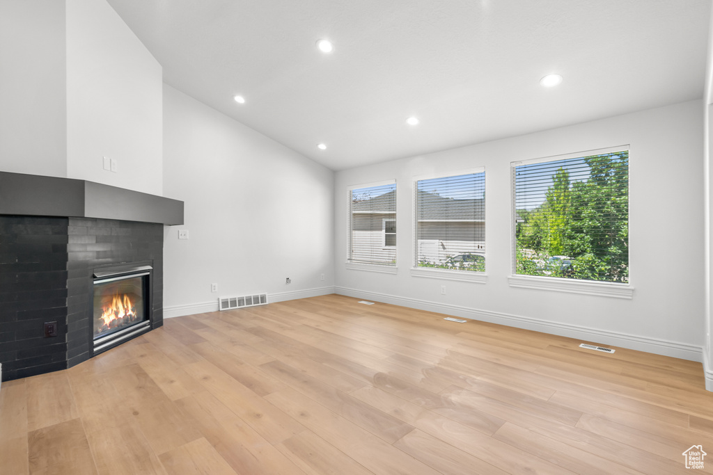 Unfurnished living room with a multi sided fireplace, light wood-style floors, recessed lighting, and vaulted ceiling