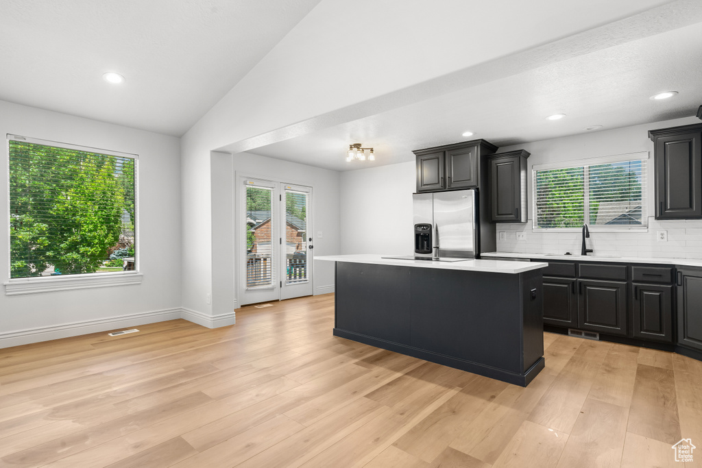 Kitchen with light countertops, a center island, decorative backsplash, lofted ceiling, and light wood finished floors