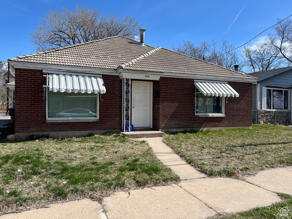 View of front of house featuring a tile roof, brick siding, and a front lawn