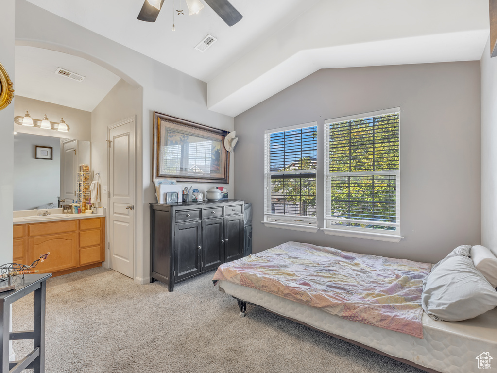Bedroom featuring vaulted ceiling, light carpet, ensuite bathroom, ceiling fan, and arched walkways