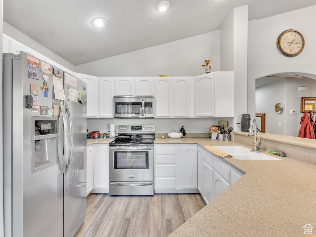 Kitchen featuring appliances with stainless steel finishes, vaulted ceiling, light wood finished floors, white cabinetry, and light countertops