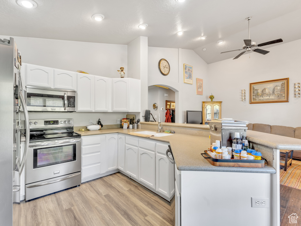 Kitchen with stainless steel appliances, a peninsula, arched walkways, vaulted ceiling, and light wood finished floors