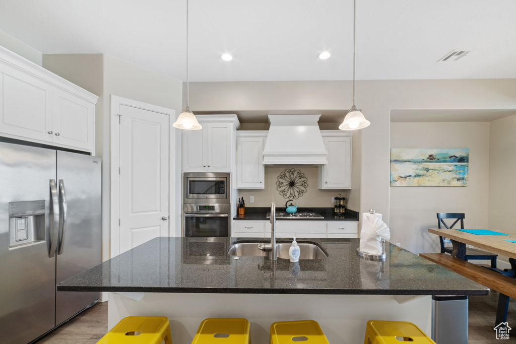 Kitchen with appliances with stainless steel finishes, custom exhaust hood, a breakfast bar, white cabinets, and recessed lighting