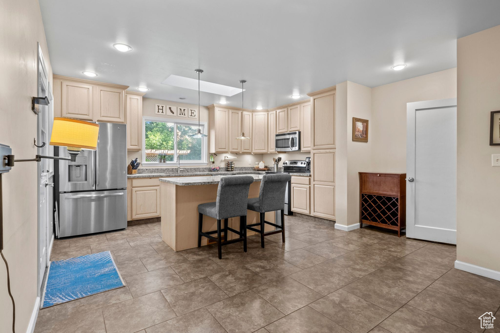 Kitchen with stainless steel appliances, a center island, a kitchen breakfast bar, decorative light fixtures, and light stone counters