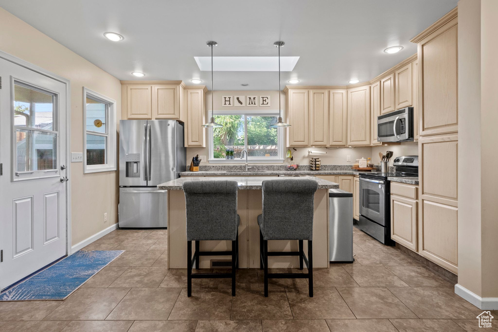 Kitchen with appliances with stainless steel finishes, a center island, a skylight, light stone counters, and a breakfast bar area