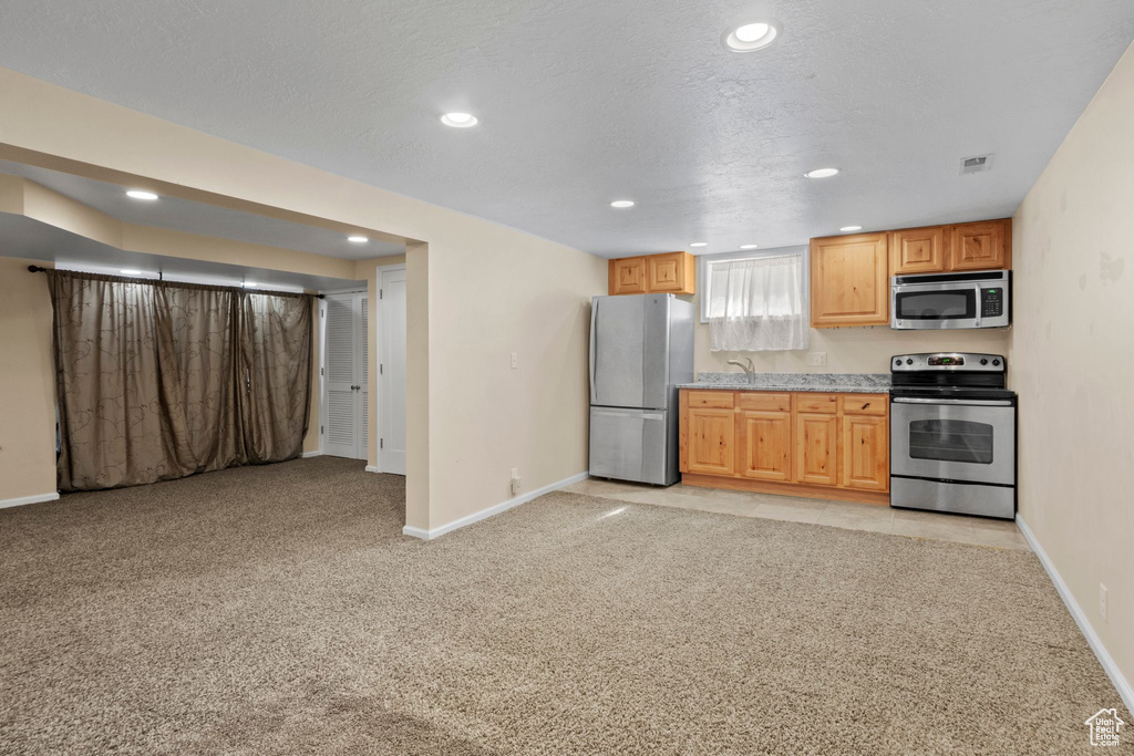 Kitchen with appliances with stainless steel finishes, recessed lighting, light colored carpet, light countertops, and open floor plan