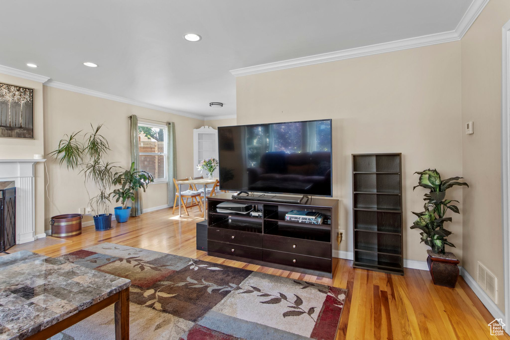 Living room with wood finished floors, ornamental molding, a premium fireplace, and recessed lighting
