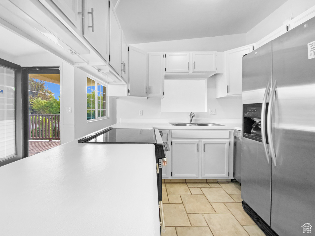 Kitchen featuring stainless steel fridge with ice dispenser, electric stove, white cabinetry, and light countertops