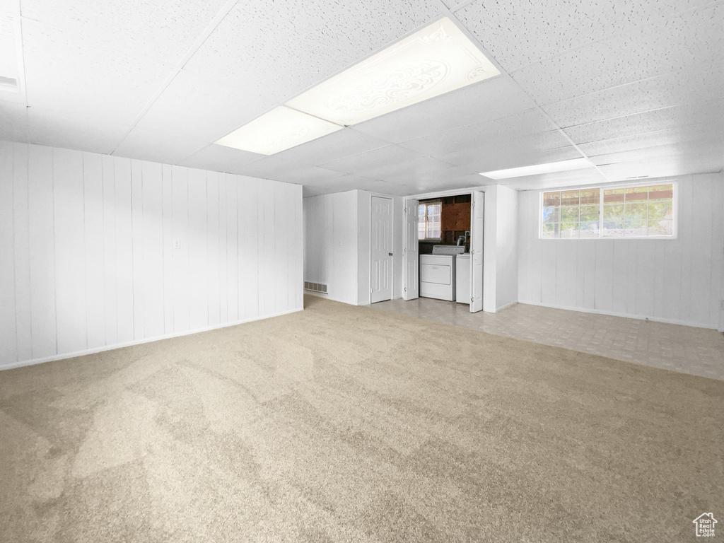 Below grade area with washing machine and dryer, carpet, wooden walls, and a drop ceiling