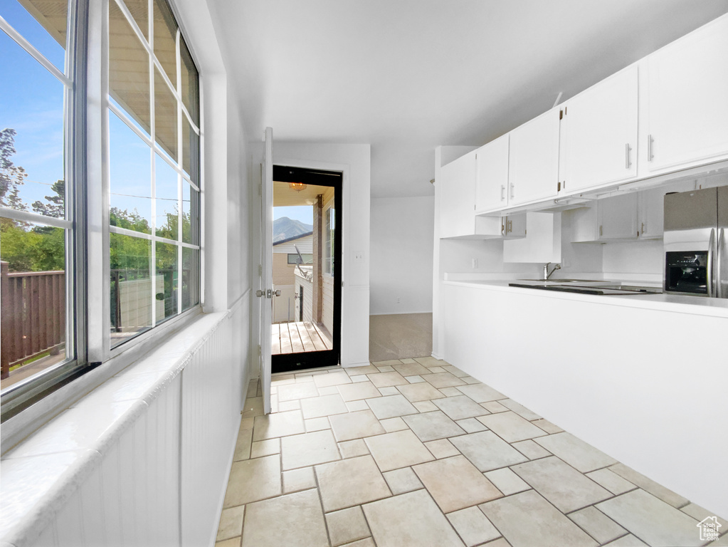Kitchen featuring stainless steel refrigerator with ice dispenser, white cabinets, light countertops, and light stone finish flooring