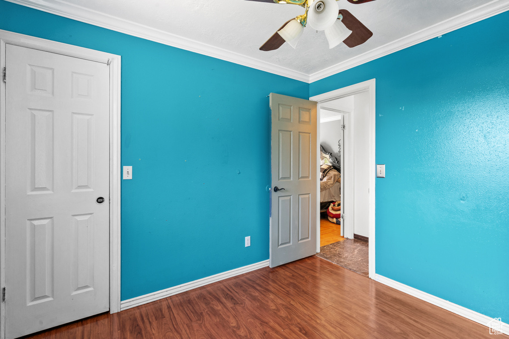 Unfurnished bedroom featuring wood finished floors, ornamental molding, and a ceiling fan
