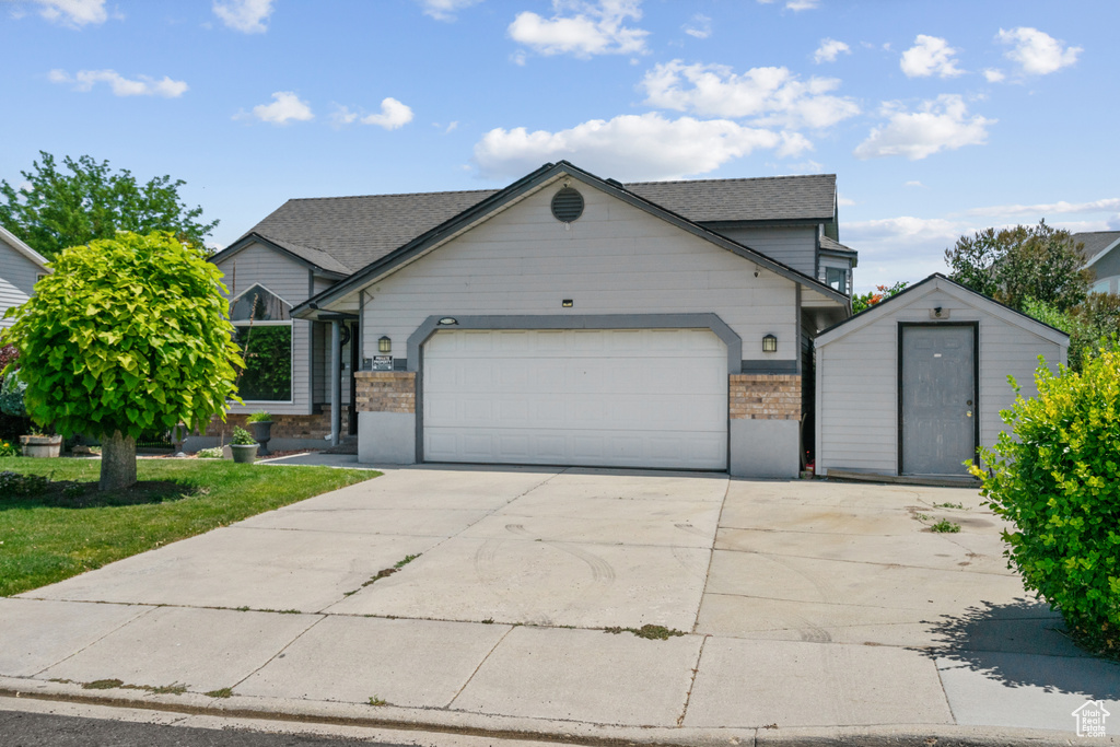 View of front of house featuring brick siding, concrete driveway, a garage, a storage unit, and a shingled roof
