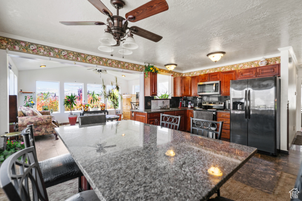 Kitchen featuring stainless steel appliances, a ceiling fan, a breakfast bar, ornamental molding, and dark stone counters