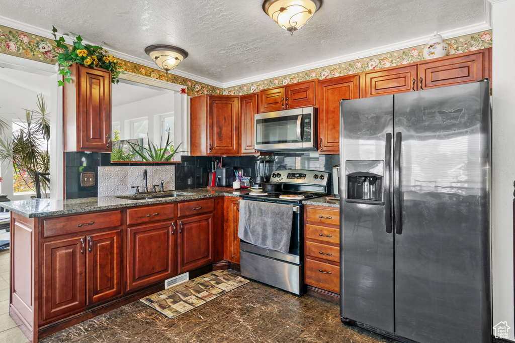 Kitchen with appliances with stainless steel finishes, a textured ceiling, tasteful backsplash, crown molding, and dark stone counters