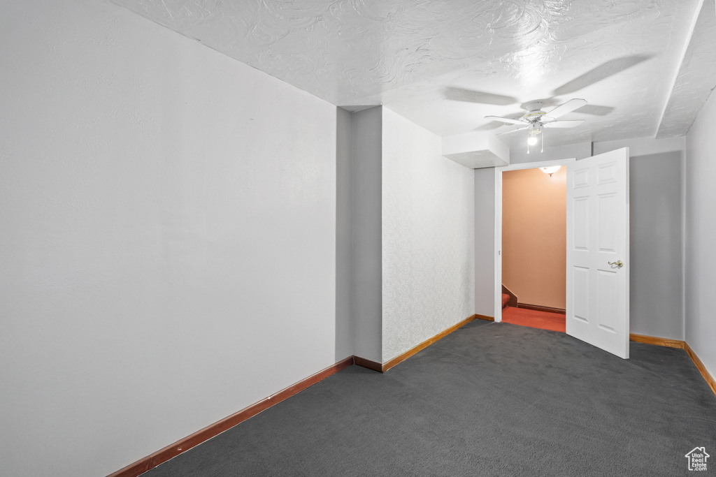 Spare room featuring a ceiling fan, dark carpet, and a textured ceiling