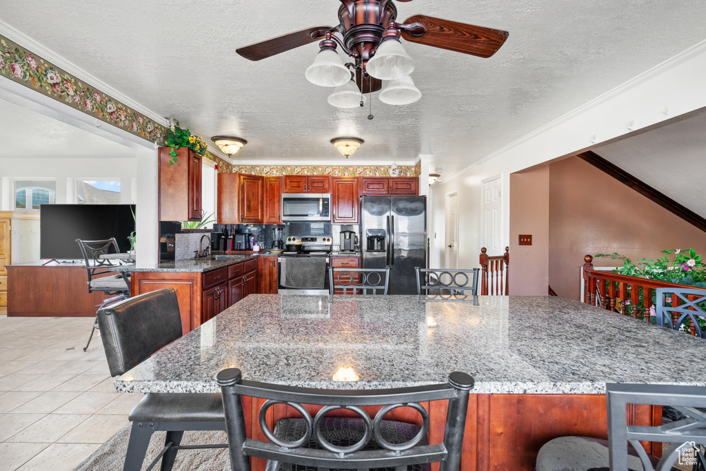 Kitchen with appliances with stainless steel finishes, a ceiling fan, a textured ceiling, ornamental molding, and a kitchen bar