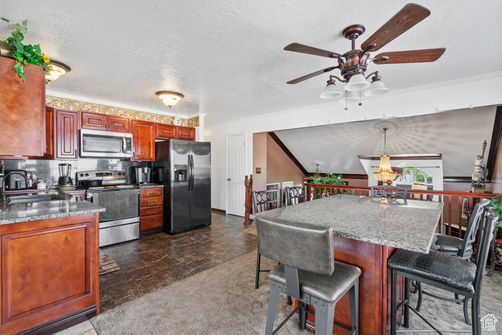 Kitchen featuring stainless steel appliances, a ceiling fan, a kitchen bar, crown molding, and dark stone countertops