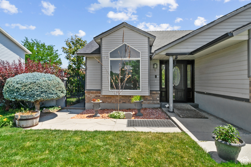 Doorway to property featuring brick siding, a gate, a shingled roof, and a lawn