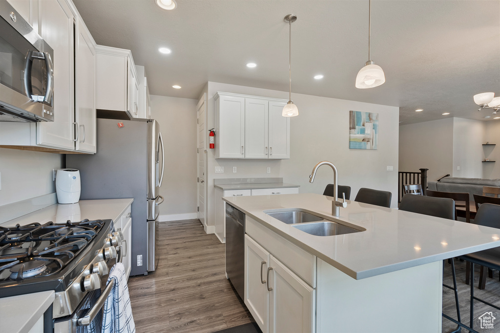Kitchen featuring stainless steel appliances, a kitchen breakfast bar, wood finished floors, light countertops, and white cabinets