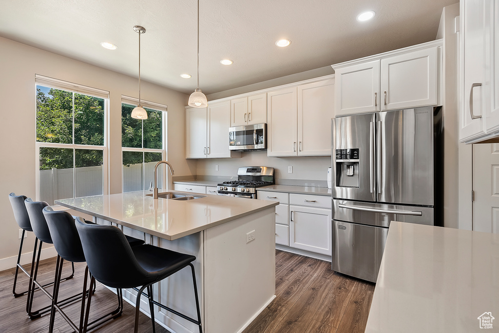 Kitchen with stainless steel appliances, dark wood-type flooring, recessed lighting, a kitchen island with sink, and white cabinets