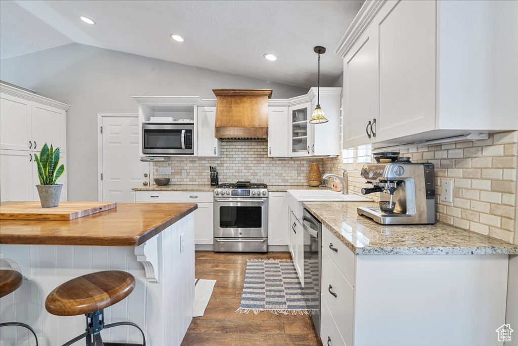 Kitchen featuring stainless steel appliances, lofted ceiling, wood counters, premium range hood, and white cabinetry