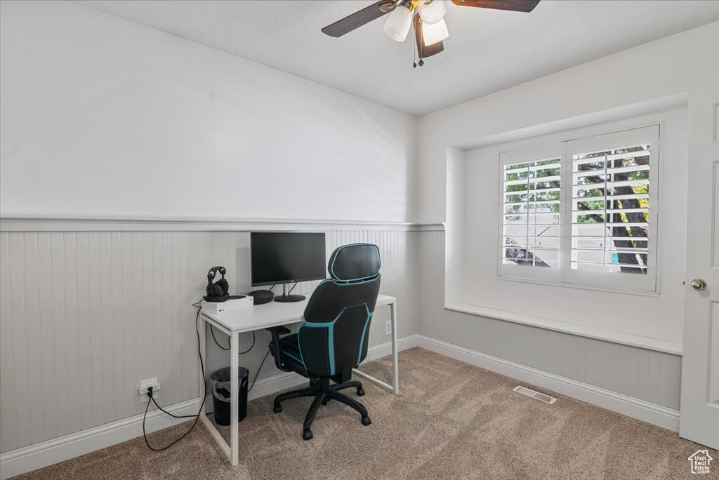 Home office featuring a wainscoted wall, carpet flooring, and ceiling fan