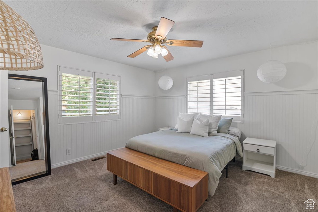 Carpeted bedroom with a wainscoted wall, a textured ceiling, and ceiling fan
