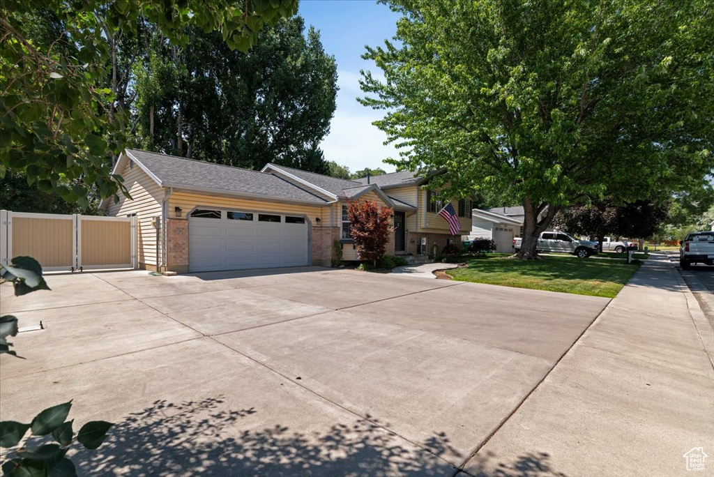 View of front of home with concrete driveway, a garage, a gate, brick siding, and a shingled roof