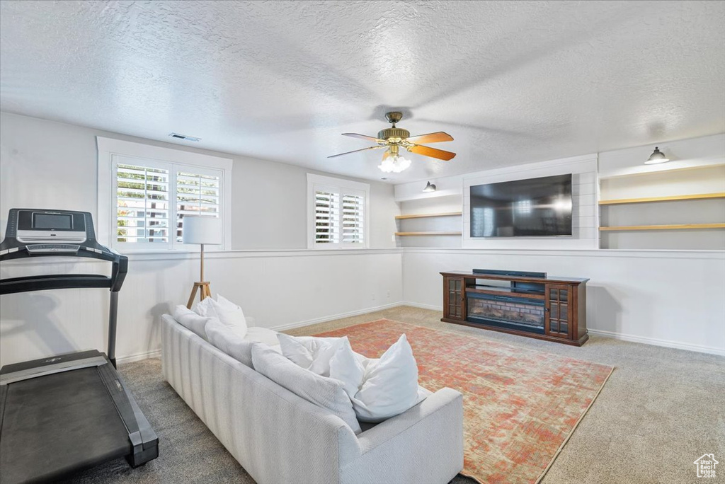 Carpeted living area with plenty of natural light, a textured ceiling, and ceiling fan
