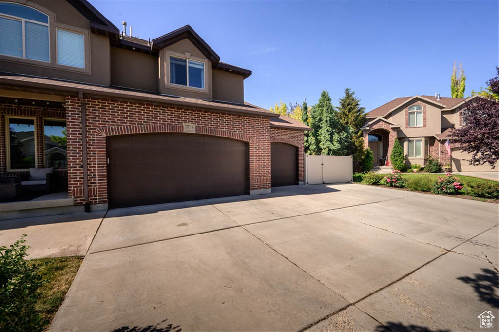 View of front of house featuring concrete driveway, brick siding, a garage, and stucco siding