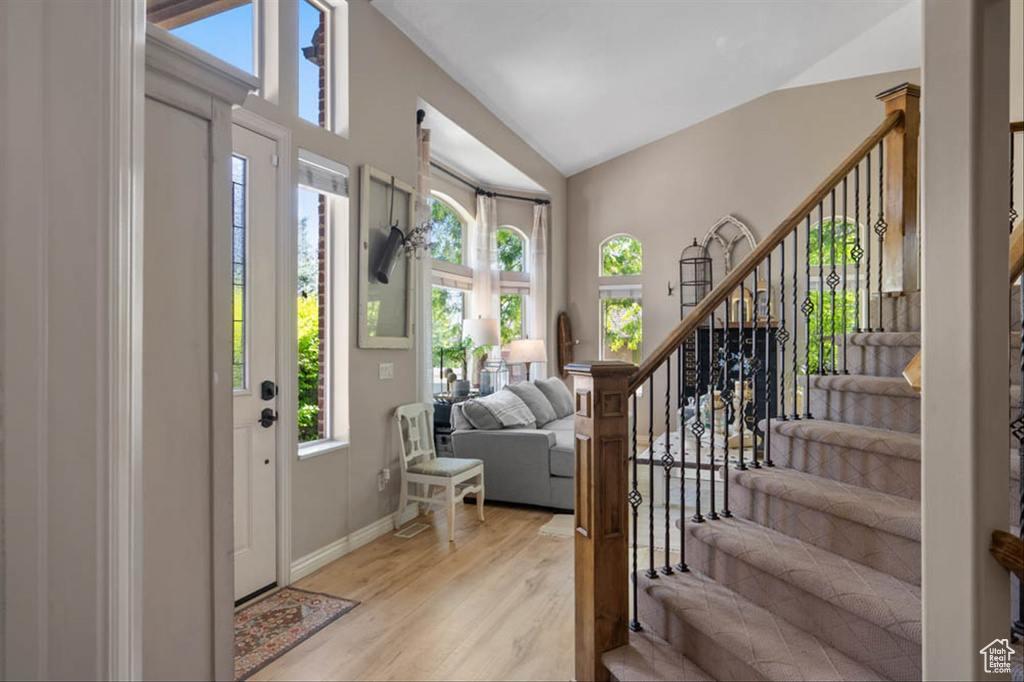 Foyer entrance featuring stairway, light wood-style flooring, and vaulted ceiling