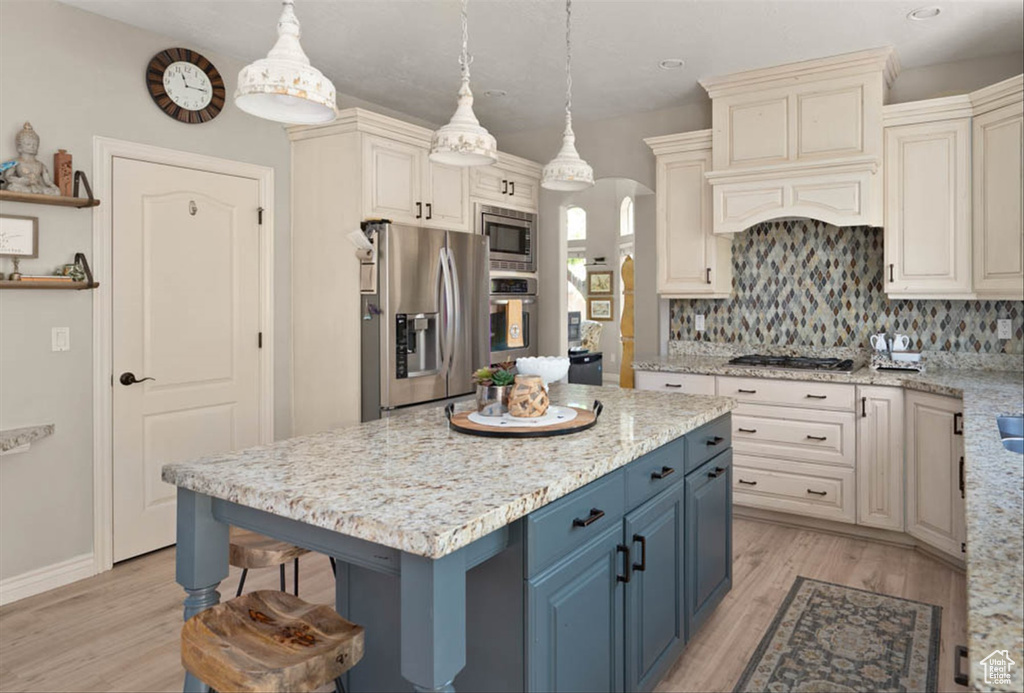 Kitchen with stainless steel appliances, blue cabinetry, light wood-style flooring, and tasteful backsplash