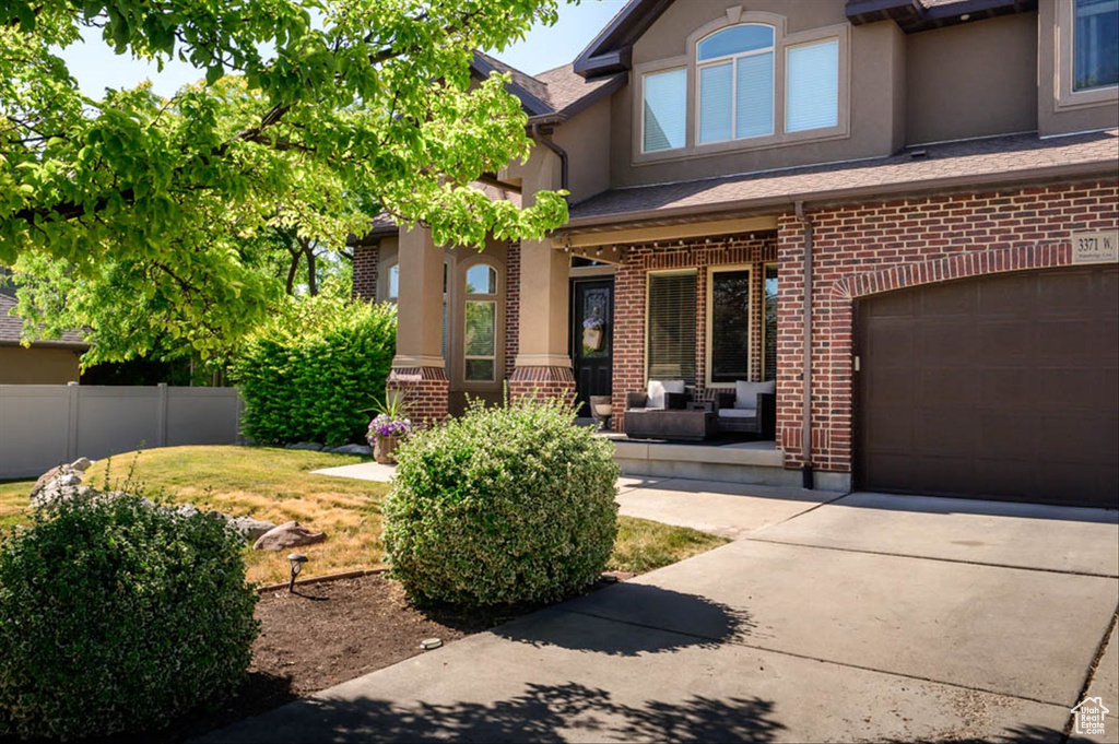 Property entrance with an attached garage, stucco siding, driveway, brick siding, and a porch