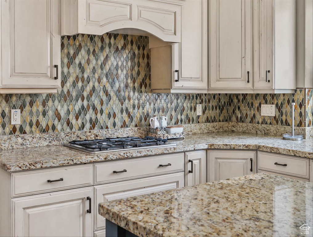 Kitchen featuring stainless steel gas stovetop, light stone counters, and decorative backsplash
