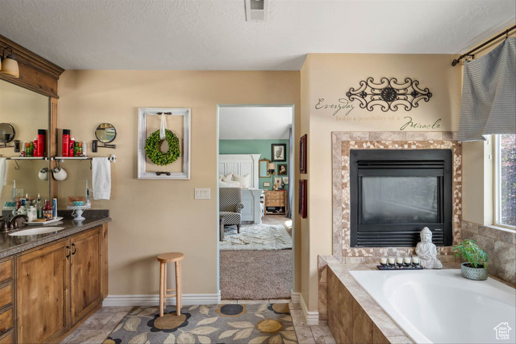 Full bath featuring vanity, a garden tub, a tiled fireplace, and ensuite bath