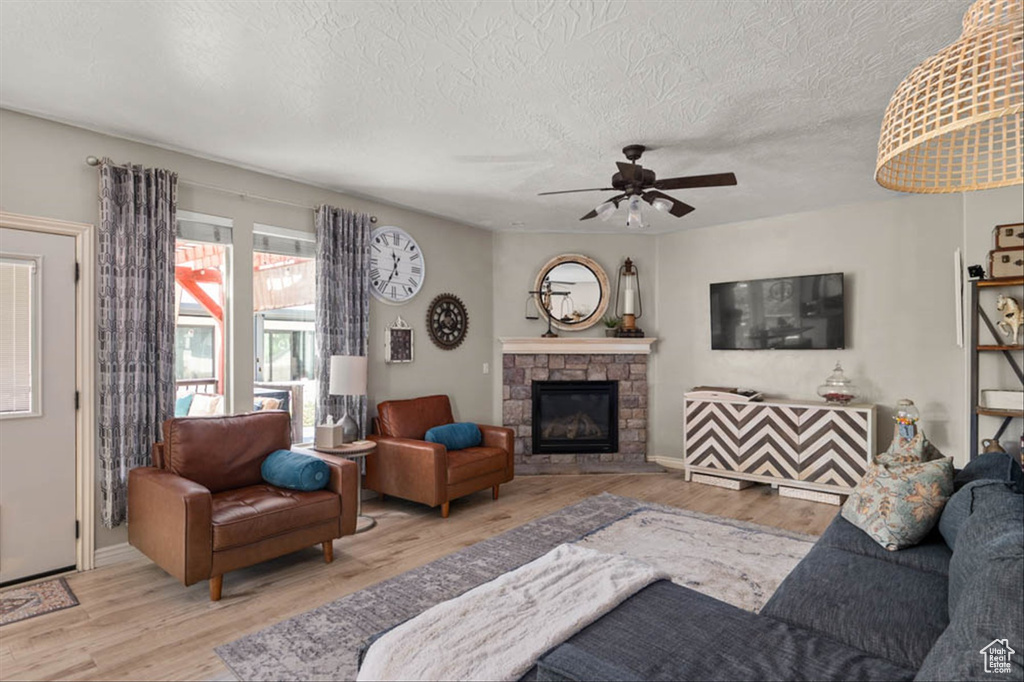 Living room featuring wood finished floors, a textured ceiling, a stone fireplace, and ceiling fan