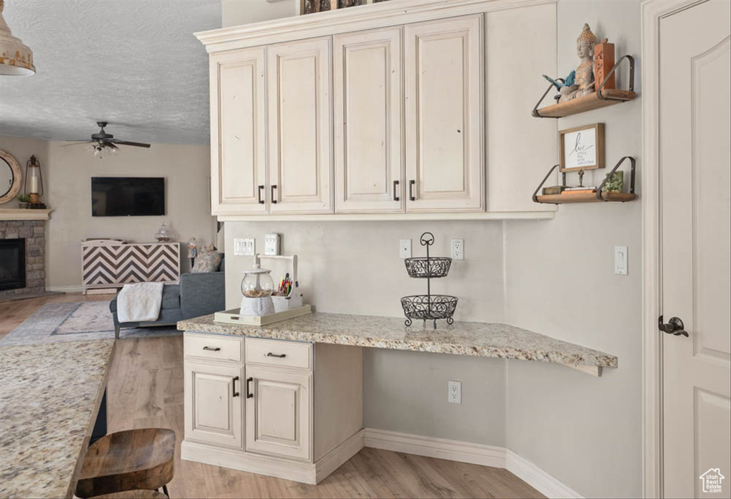 Kitchen featuring light wood-style floors, ceiling fan, open floor plan, cream cabinets, and light stone counters