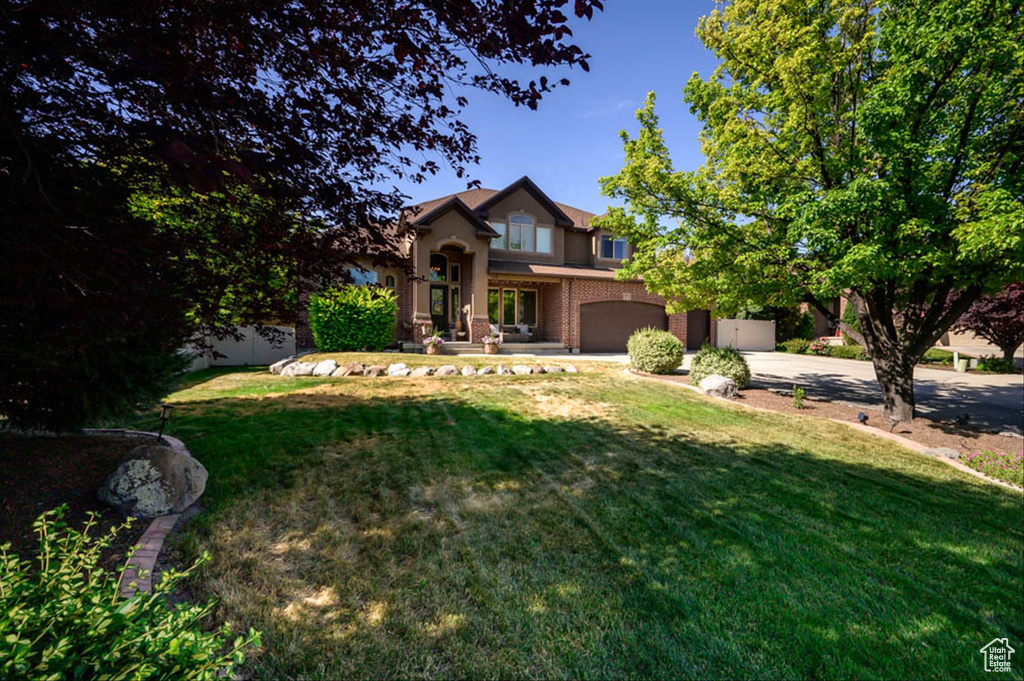 Traditional-style home featuring an attached garage, driveway, a front yard, and brick siding