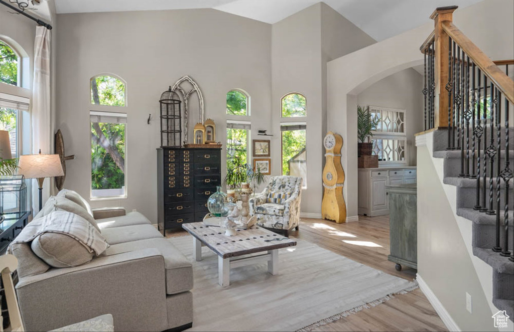 Living area with arched walkways, light wood-style floors, stairway, and high vaulted ceiling