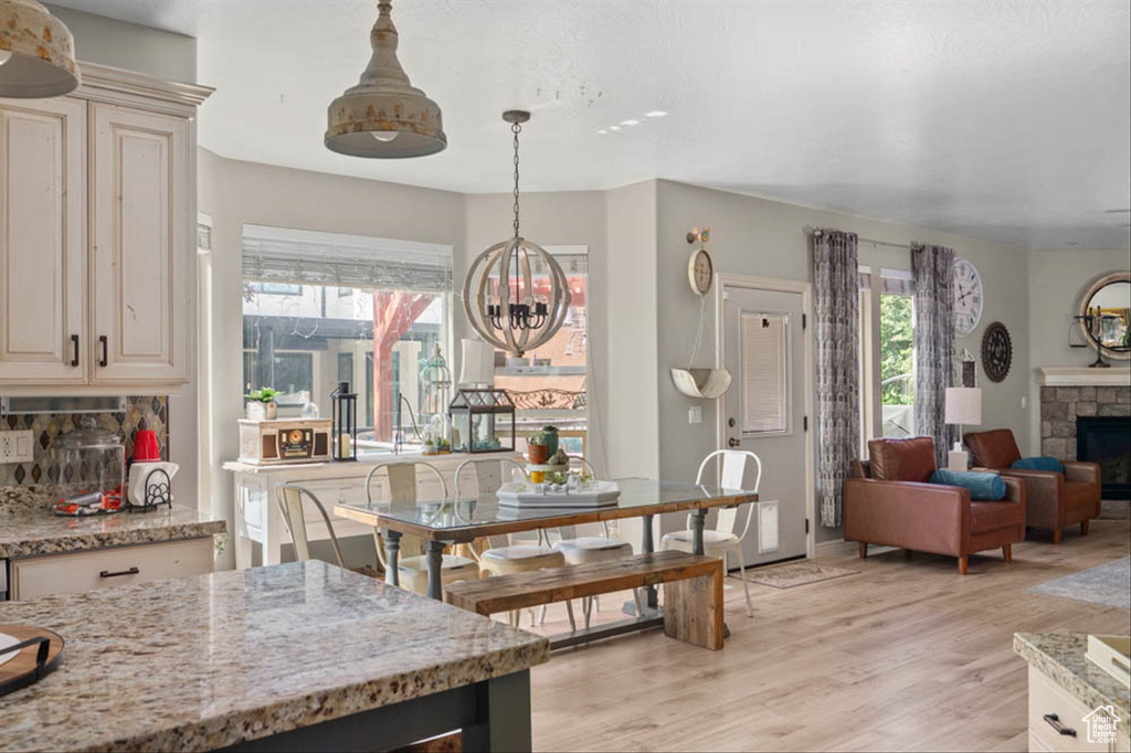 Dining area with a chandelier, light wood-style floors, and a stone fireplace