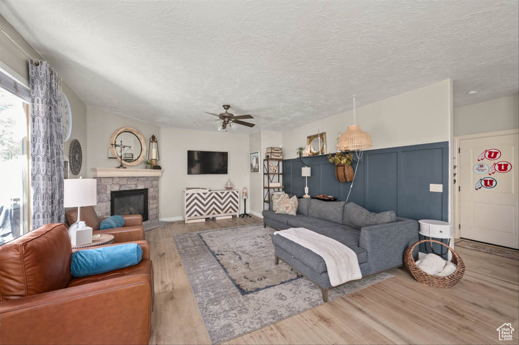 Living room featuring wood finished floors, ceiling fan, a fireplace, and a textured ceiling